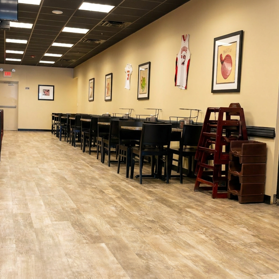 Empty restaurant dining room with red booths, rows of tables, framed artwork, sports jerseys, and warm overhead lighting.