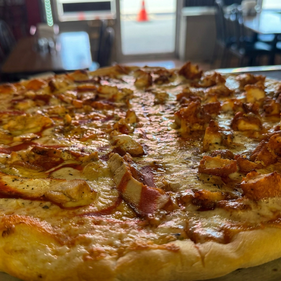 Large golden-crusted pizza topped with melted cheese, pepperoni, mushrooms, and browned chicken on a metal tray in a restaurant.